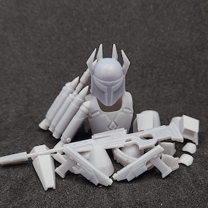 Könnte beinhalten: Ein weißes Plastik-Actionfiguren-Set mit Helm, Torso und verschiedenen Waffen. Die Figur ist ein mandalorianischer Krieger mit einem Helm, der mit einer Kämme und einem Visier verziert ist.