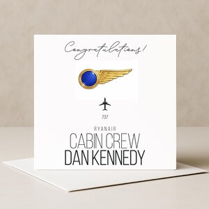 May include: A white greeting card with the word "Congratulations!" in cursive. The card features a gold and blue pin of wings and a plane icon. Text on the card reads "Ryanair Cabin Crew Dan Kennedy".