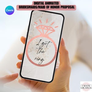 以下が含まれることがあります： スマートフォン画面に表示されたデジタルグラフィック。ローズゴールドのグリッターダイヤモンドリングのイラストと、黒い筆記体で書かれた「I got the ring」というテキスト。背景は柔らかな白い布の質感で、繊細な光の演出が施されている。