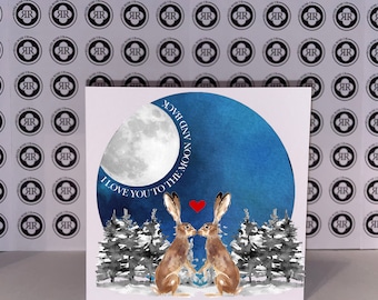 Puede incluir: Una tarjeta de felicitación con una ilustración de acuarela de dos liebres mirándose bajo una luna azul. El texto "Te amo hasta la luna y de regreso" está escrito alrededor de la luna.