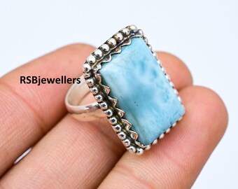 Könnte beinhalten: Ein silberner Ring mit einem hellblauen Edelstein, der in einen Perlenrand gefasst ist. Der Edelstein hat eine wolkig-marmorierte Optik.