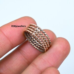 May include: Five thin, twisted, silver rings with a rose gold finish. The rings are stacked on top of each other and are being held by a hand.