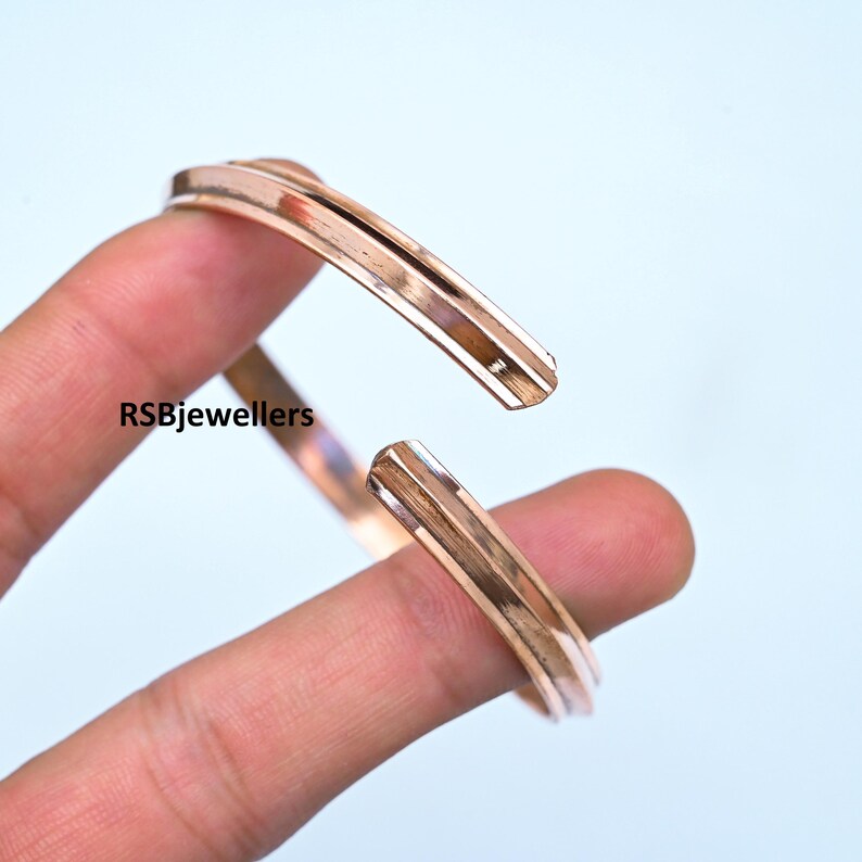 May include: A rose gold bangle bracelet with a simple, elegant design. The bracelet is open and has a slightly curved shape.