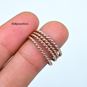 May include: Set of four thin, twisted copper rings. The rings are stacked on top of each other and are worn on a finger.