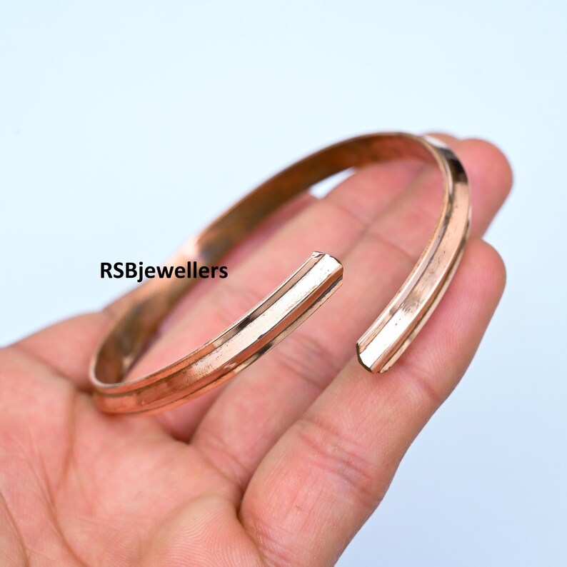 May include: A simple copper bangle bracelet with a slightly rounded edge. The bracelet is open and has a slightly textured surface.