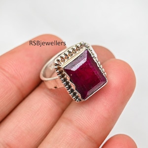 Può includere: Un anello d'argento con una grande pietra preziosa quadrata di colore rosso scuro incastonata in un bordo perlato.