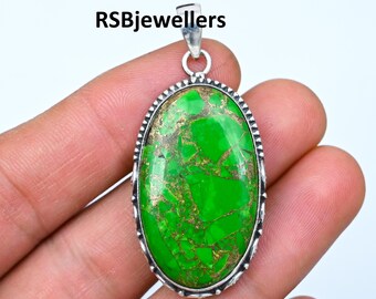 Puede incluir: Un colgante de plata con una gran piedra ovalada de turquesa verde con motas doradas. La piedra está engastada en un bisel de plata con un borde decorativo.