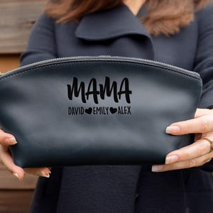 May include: Black leather makeup bag with a zipper closure. The bag has the word "MAMA" written in a stylized font with the names "David", "Emily", and "Alex" written below it, each name separated by a heart.
