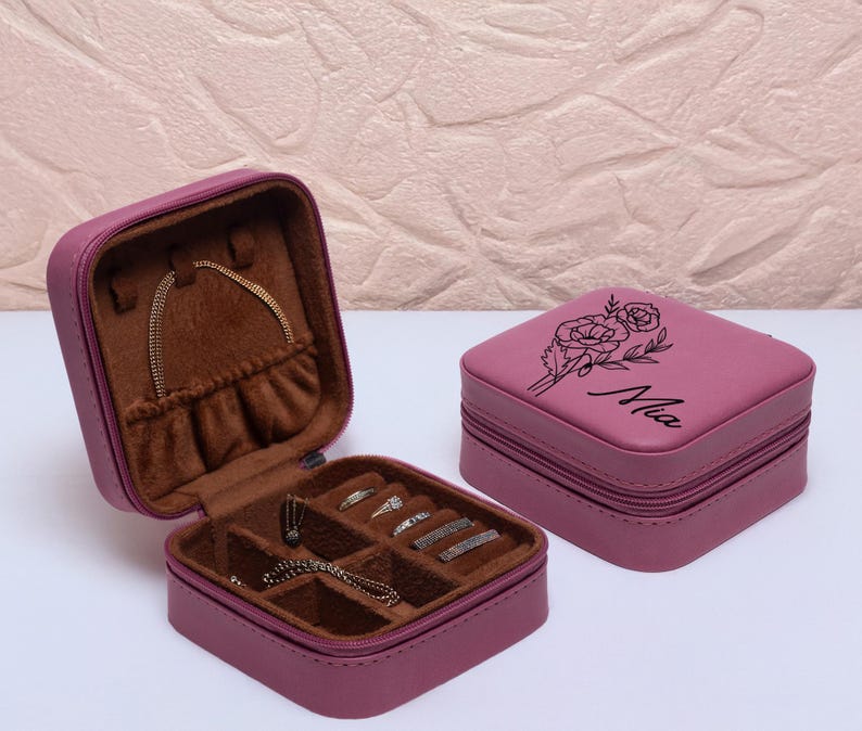 Puede incluir: Una caja de joyer&iacute;a de dos niveles con un dise&ntilde;o floral y el nombre "Mia" grabado en la parte superior. La caja est&aacute; hecha de piel sint&eacute;tica y tiene un color rosa.