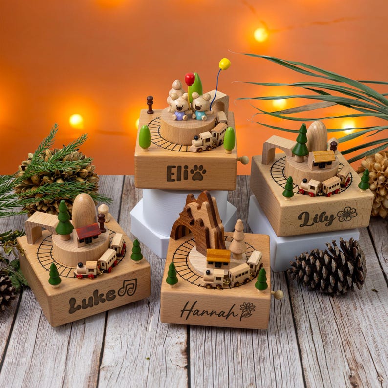 Może przedstawiać: Cztery drewniane pozytywki z motywami pociąg&oacute;w i tor&oacute;w. Każde pudełko ma inną nazwę: Eli, Lily, Luke i Hannah. Pudełka mają miniaturowe drzewa, g&oacute;ry i figurki niedźwiedzi. Pudełko Eli ma odcisk łapy, a pudełko Lily ma kwiat.