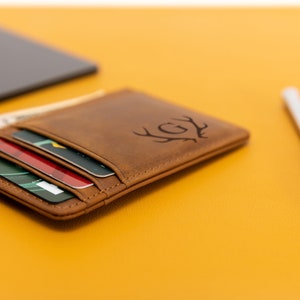 May include: A brown leather card holder with a monogrammed design of a deer's antlers and the initials "GY". The card holder is open and has several cards inside.