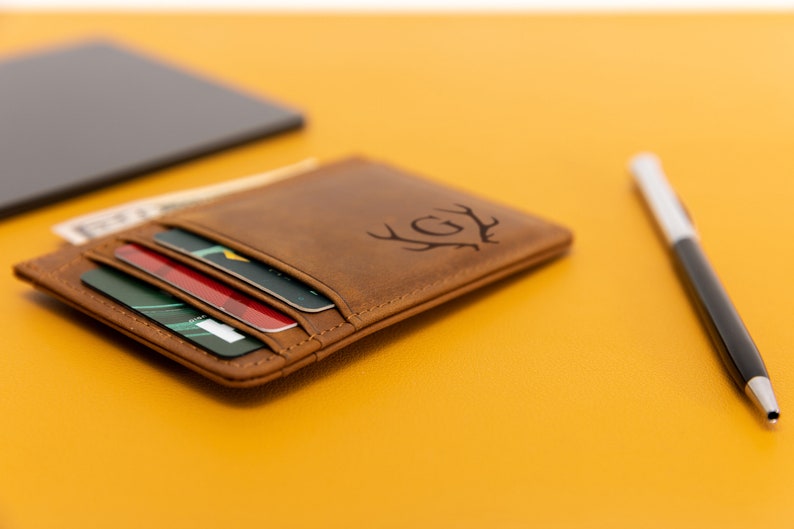May include: A brown leather card holder with a monogrammed design of a deer's antlers and the initials "GY". The card holder is open and has several cards inside.