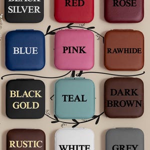 Puede incluir: Doce cajas cuadradas para anillos en varios colores, incluyendo negro, rojo, rosa, azul, rosa, cuero crudo, oro negro, turquesa, marr&oacute;n oscuro, oro r&uacute;stico, blanco y gris. Cada caja tiene un color diferente y una etiqueta de texto que indica el color.