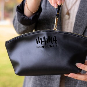 May include: Black zippered makeup bag with a gold zipper. The bag has the word "MAMA" written in a script font with three hearts and the names "DAVID", "EMILY", and "ALEX" underneath.