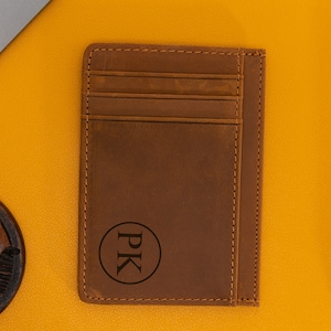 May include: A brown leather card holder with a stitched edge and a circle monogrammed with the initials "PK".