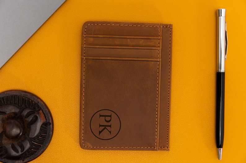 May include: A brown leather card holder with a stitched edge and a circle monogrammed with the initials "PK".