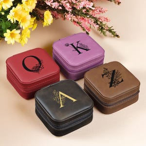 Puede incluir: Cuatro peque&ntilde;as cajas cuadradas de joyer&iacute;a con diferentes exteriores de piel sint&eacute;tica de colores. Cada caja tiene una letra diferente en la parte superior, A, K, O y Z, con un dise&ntilde;o floral. Las cajas est&aacute;n todas cerradas.