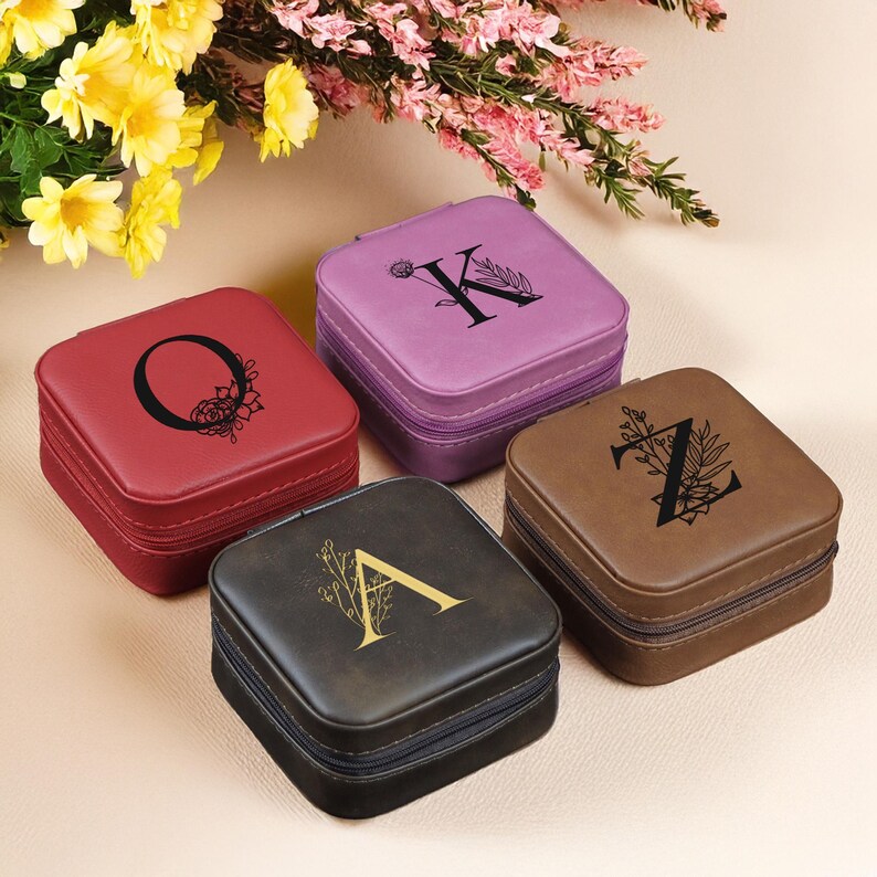 Puede incluir: Cuatro peque&ntilde;as cajas cuadradas de joyer&iacute;a con diferentes exteriores de piel sint&eacute;tica de colores. Cada caja tiene una letra diferente en la parte superior, A, K, O y Z, con un dise&ntilde;o floral. Las cajas est&aacute;n todas cerradas.
