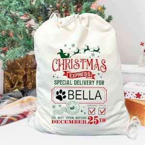 May include: A white canvas Santa sack with a red and green Christmas Express design. The sack has a personalized name tag that says "BELLA" and the text "DO NOT OPEN BEFORE DECEMBER 25TH".