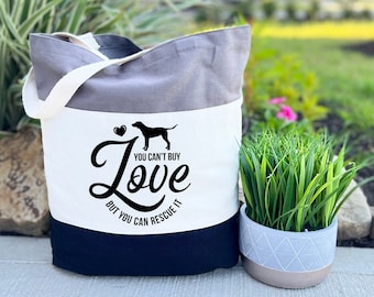 May include: A tri-color tote bag with a black silhouette of a dog and the text "You can't buy love but you can rescue it".