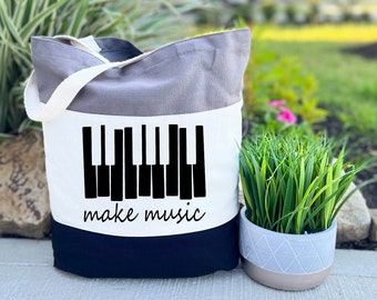 Peut inclure: Un sac fourre-tout tricolore avec un motif de clavier de piano noir et blanc et le texte "make music". Le sac est gris, blanc et noir.