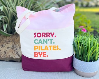 May include: A pink, white, and burgundy tote bag with the text "SORRY. CAN'T. PILATES. BYE." printed on the front.