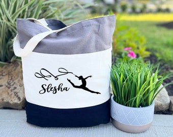 May include: A tri-color tote bag with a gray, white, and black design. The bag features a gymnast silhouette and the name "Slesha" in cursive.