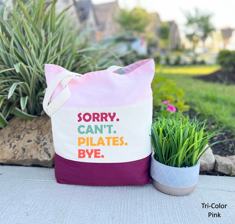 May include: A pink, white, and burgundy tote bag with the text "SORRY. CAN'T. PILATES. BYE." printed on the front.