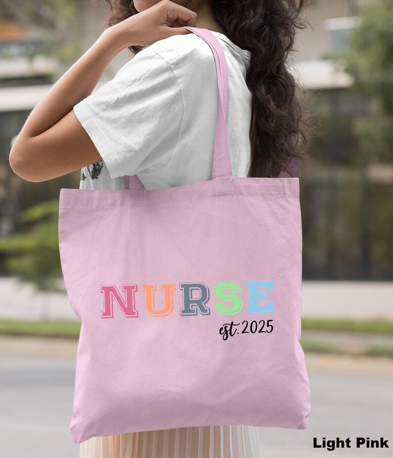 May include: Light pink tote bag with the word "NURSE" in rainbow colours and the text "est. 2025" underneath.