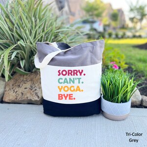 Puede incluir: Una bolsa de lona gris, blanca y negra con el texto "SORRY. CAN'T. YOGA. BYE." en letras de colores.