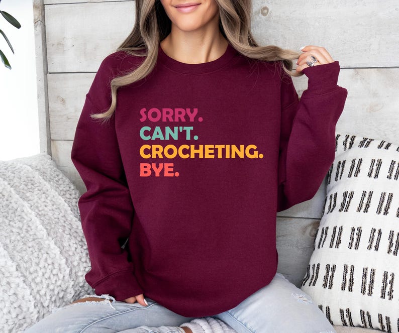 May include: A maroon sweatshirt with the text "SORRY. CAN'T. CROCHETING. BYE." in colorful letters.