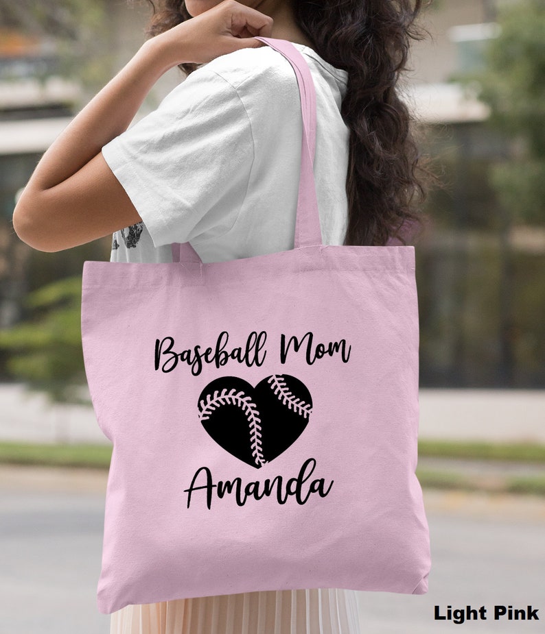 May include: A light pink tote bag with black text that reads "Baseball Mom" and a black heart with a baseball inside. The name "Amanda" is written below the heart.