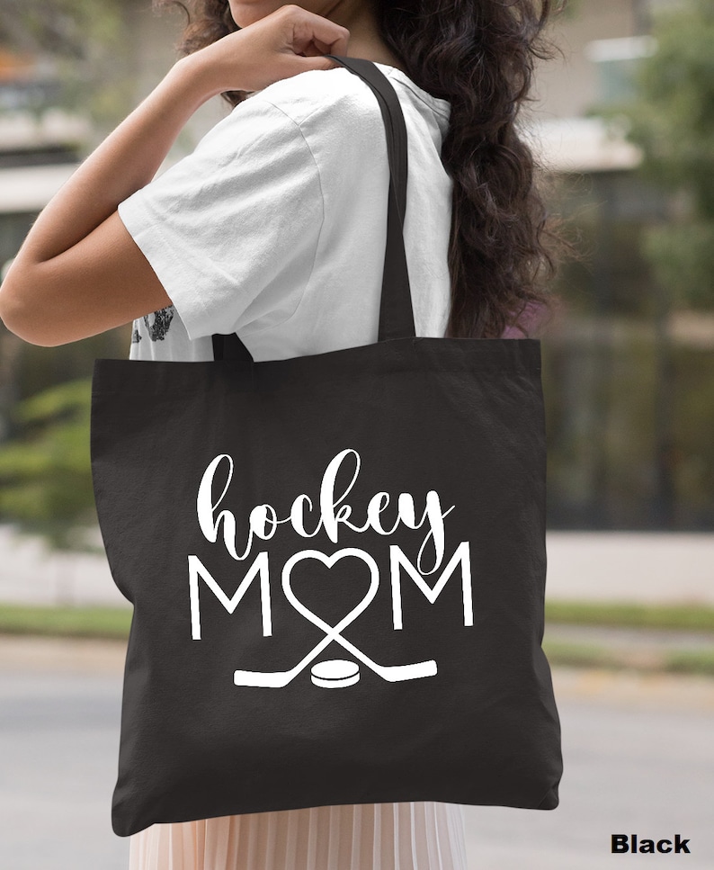 May include: Black canvas tote bag with white text that reads "hockey MOM" with a heart replacing the "O".  Two hockey sticks and a puck are below the text.