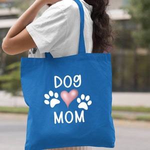 May include: A royal blue tote bag with white text that says "Dog Mom" and a pink heart with white paw prints on either side of the heart.