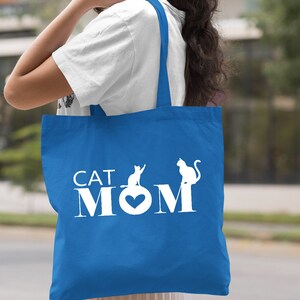 Peut inclure: Un sac fourre-tout bleu royal avec des poign&eacute;es blanches et le texte "CAT MOM" en blanc avec deux silhouettes de chats blanches.