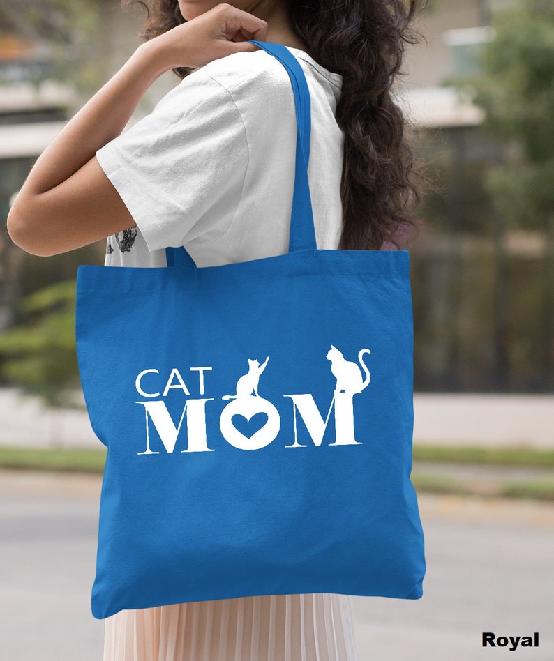 Peut inclure: Un sac fourre-tout bleu royal avec des poign&eacute;es blanches et le texte "CAT MOM" en blanc avec deux silhouettes de chats blanches.