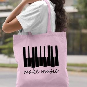 May include: A light pink tote bag with a black piano keyboard graphic and the text "make music".