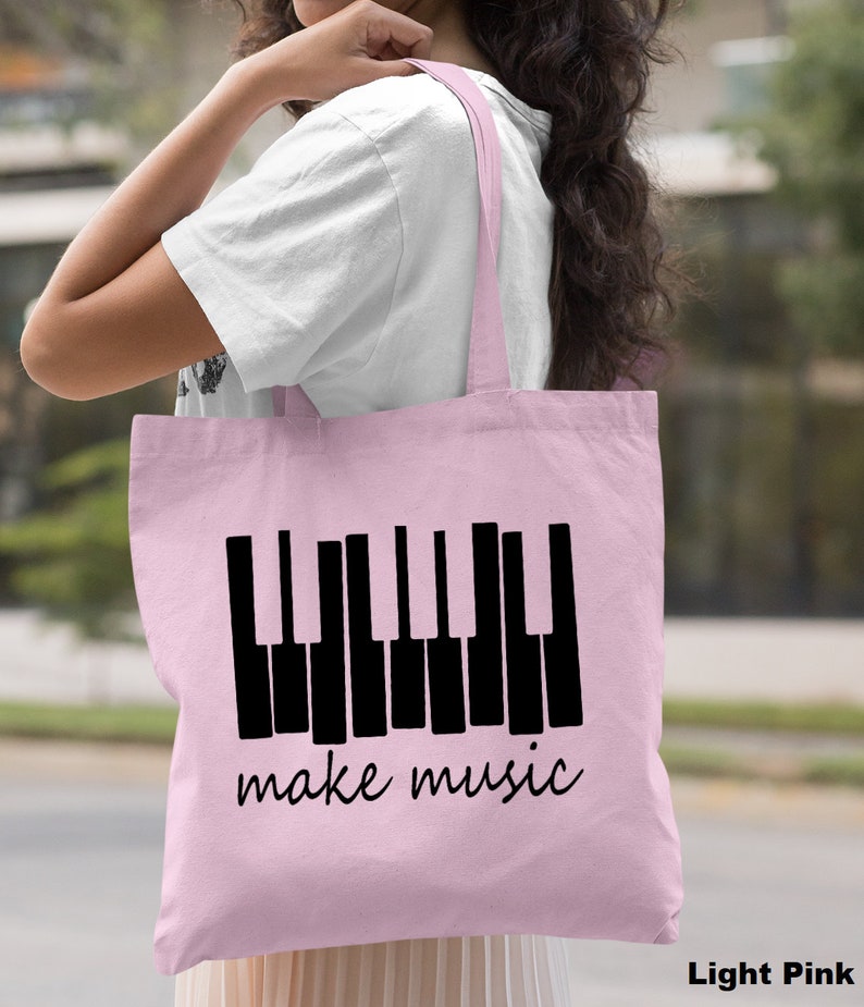 May include: A light pink tote bag with a black piano keyboard graphic and the text "make music".