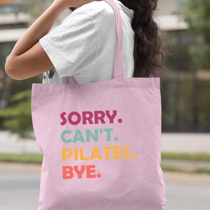 May include: A light pink tote bag with the text "SORRY. CAN'T. PILATES. BYE." in colorful letters.