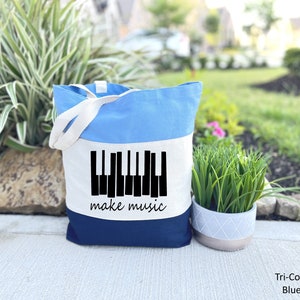 May include: A blue, white, and navy blue tote bag with a black piano keyboard graphic and the text "make music".