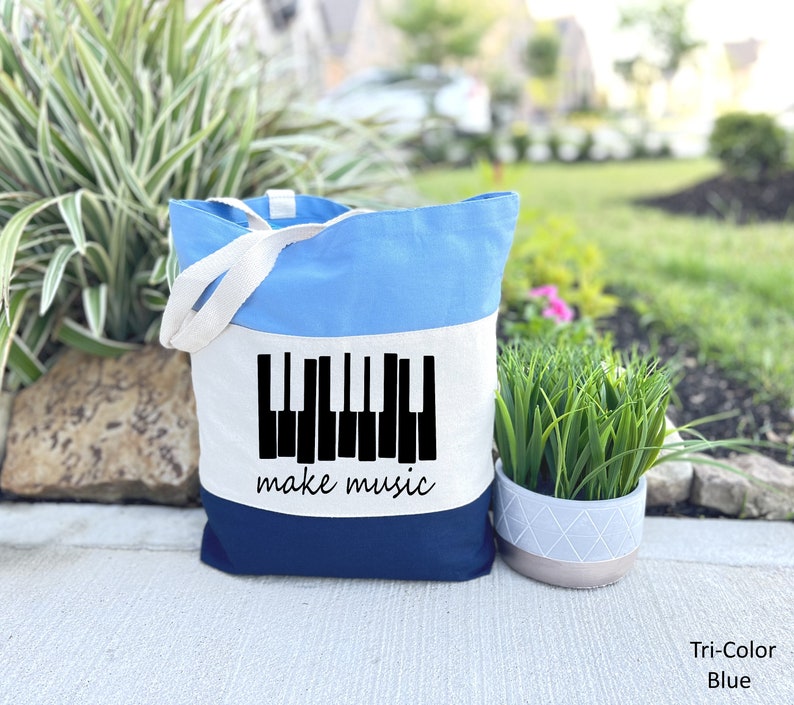 May include: A blue, white, and navy blue tote bag with a black piano keyboard graphic and the text "make music".