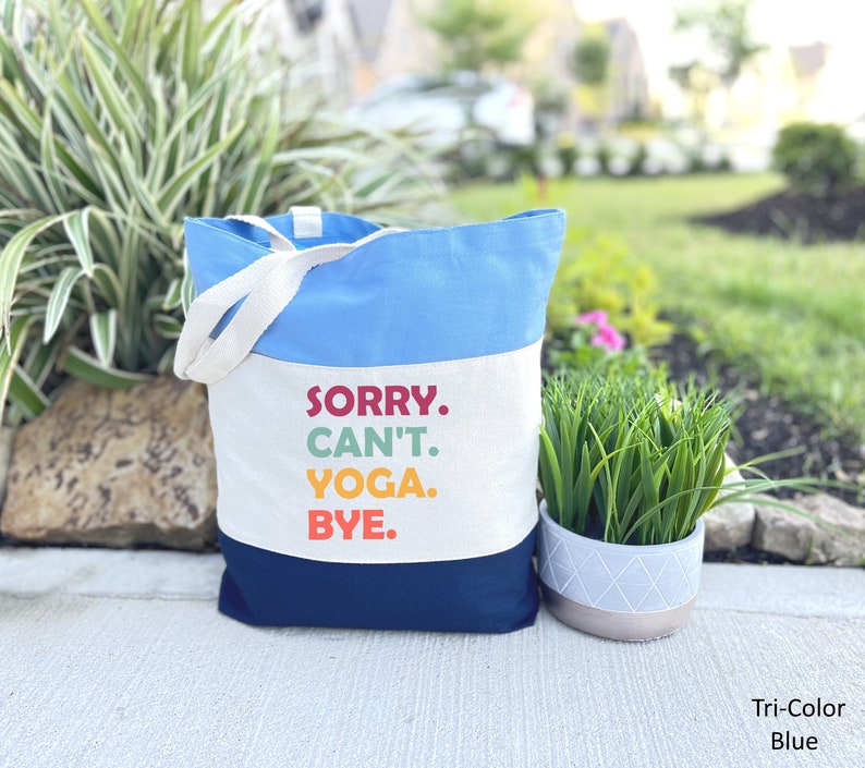 Puede incluir: Una bolsa de lona azul y blanca con el texto "SORRY. CAN'T. YOGA. BYE." en letras de colores. La bolsa tiene una secci&oacute;n superior azul y una secci&oacute;n inferior azul marino.