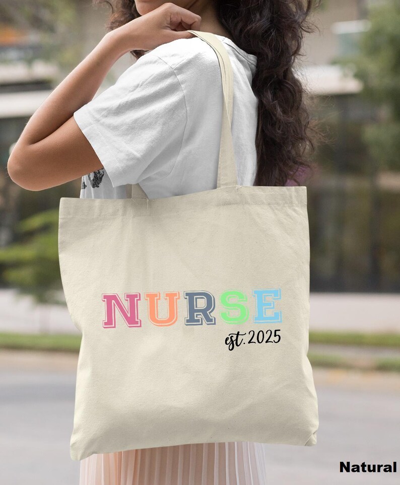 May include: A natural canvas tote bag with the word "NURSE" in rainbow colours and the text "est. 2025" in black.