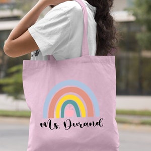 Puede incluir: Bolsa de tela rosa claro con un dise&ntilde;o de arco&iacute;ris y el texto "Ms. Durand".