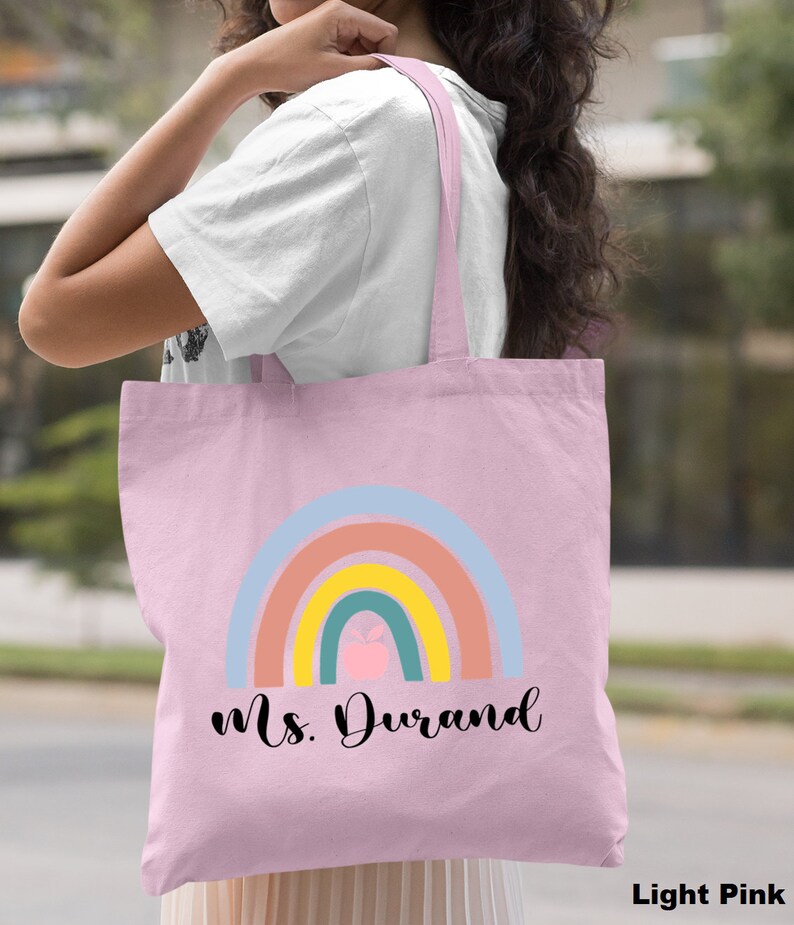Puede incluir: Bolsa de tela rosa claro con un dise&ntilde;o de arco&iacute;ris y el texto "Ms. Durand".
