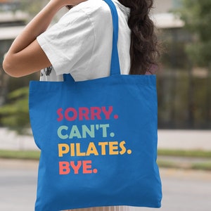 May include: A royal blue tote bag with the text "SORRY. CAN'T. PILATES. BYE." in colorful letters.