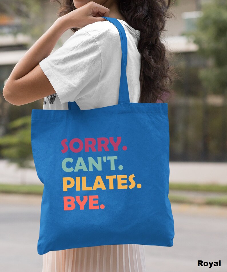 May include: A royal blue tote bag with the text "SORRY. CAN'T. PILATES. BYE." in colorful letters.