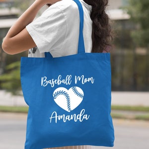 May include: A royal blue tote bag with white text that reads "Baseball Mom Amanda" and a white baseball in a heart shape.