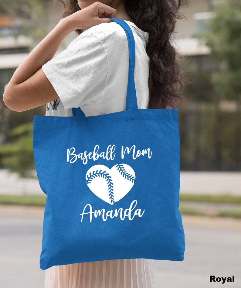 May include: A royal blue tote bag with white text that reads "Baseball Mom Amanda" and a white baseball in a heart shape.