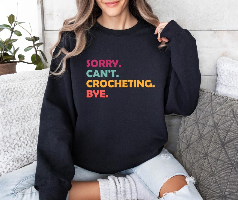 May include: A black sweatshirt with the text "SORRY. CAN'T. CROCHETING. BYE." in colorful letters.